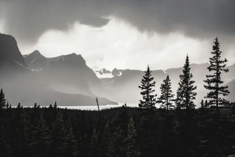 the mountains are behind trees and dark clouds in the distance