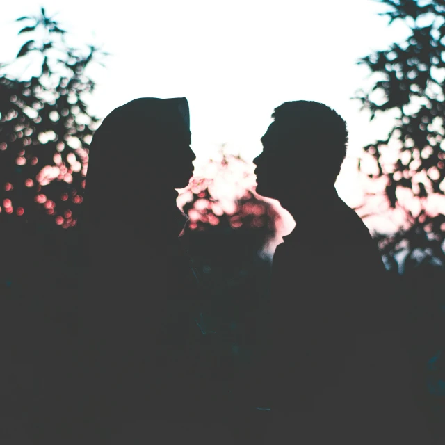 two people are silhouetted against trees in the sunlight