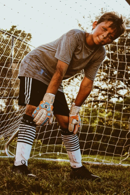 a person in black shorts and gray shirt and white socks holding a soccer ball in front of goal