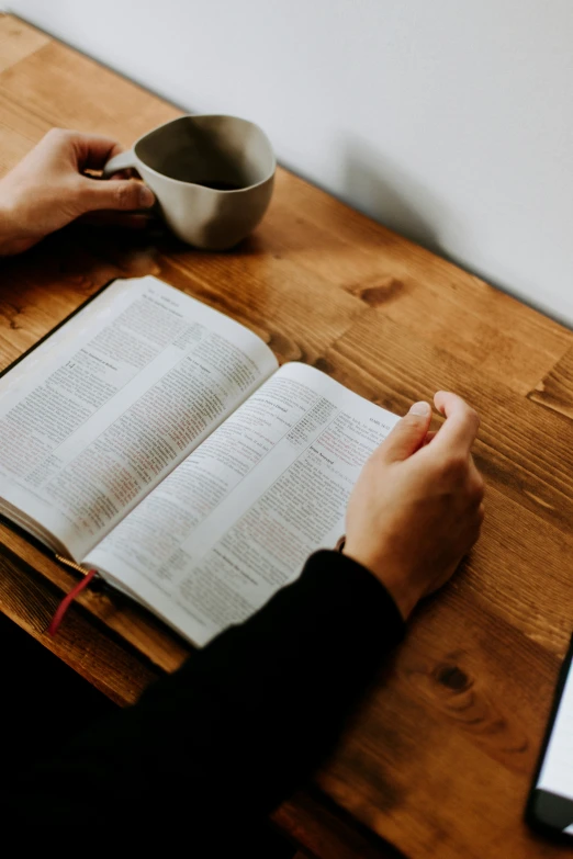 an open bible, on the table, with someone's hands