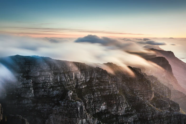 clouds over the top of mountains rise above a body of water