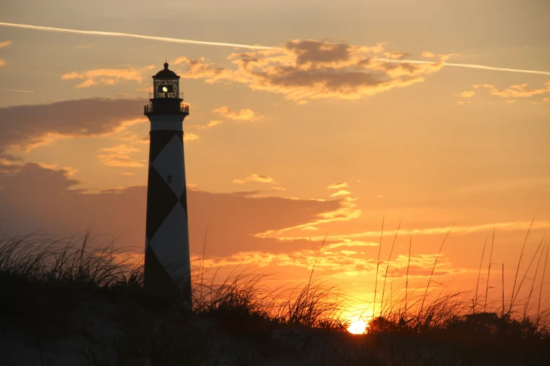 a black and white lighthouse on a beach at sunset