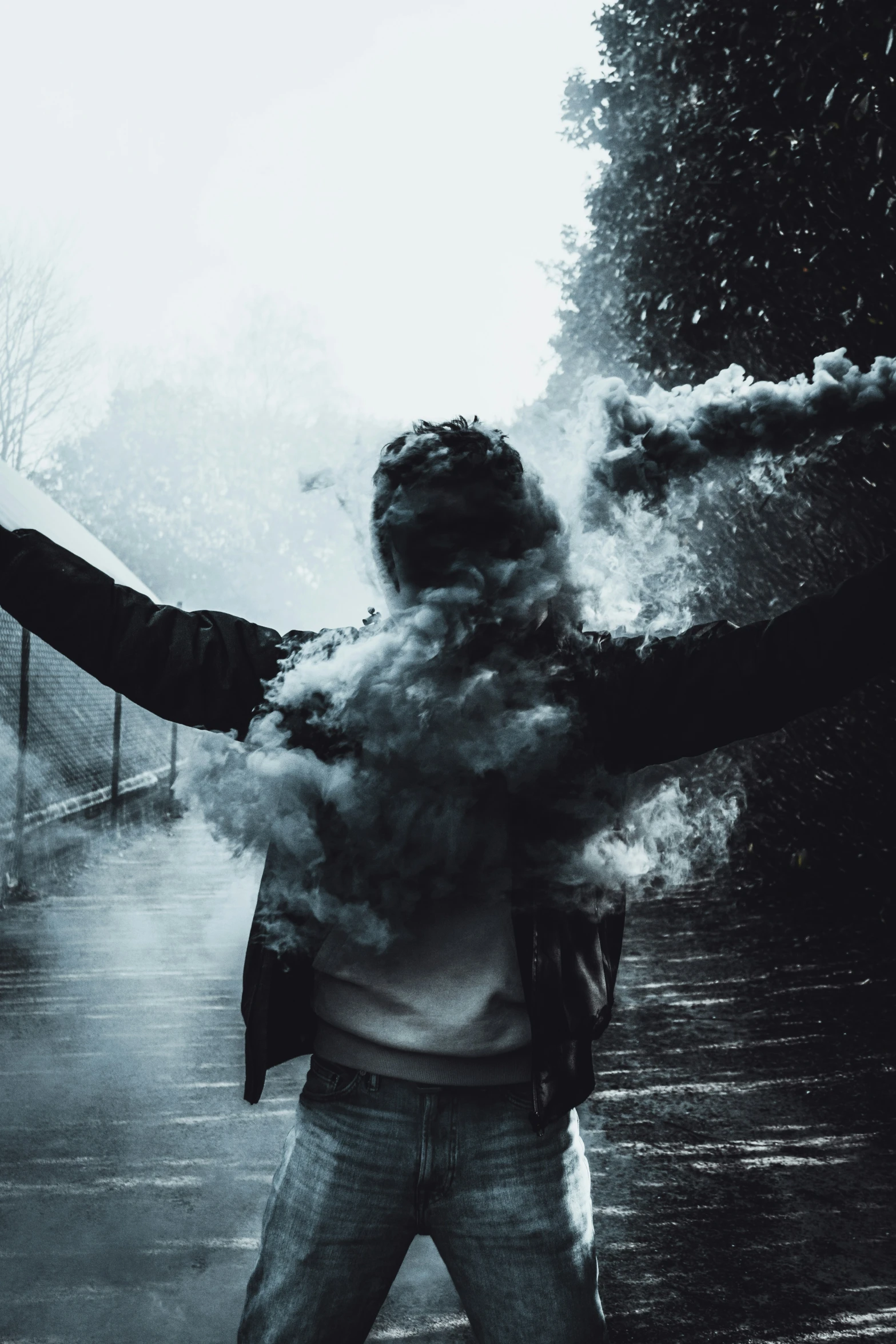 person standing on road with their arms out as smoke billows