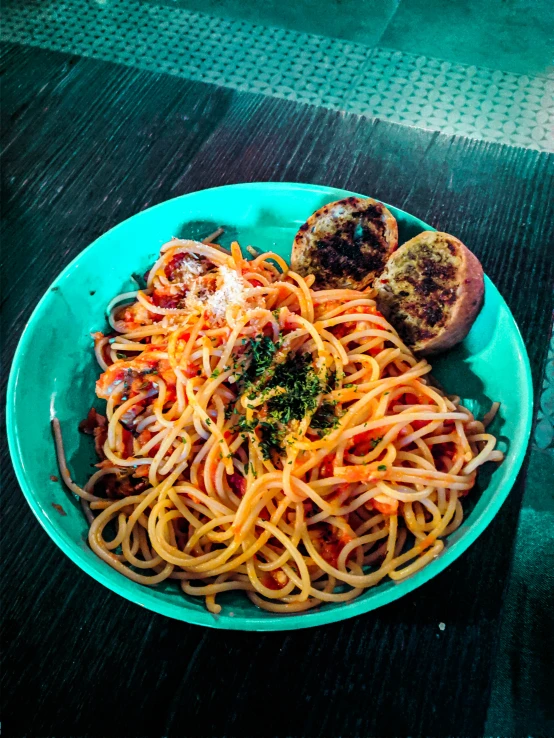 a bowl of spaghetti on a table with some bread