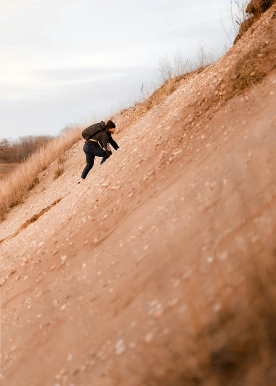 a man walking up the side of a hill with grass on top