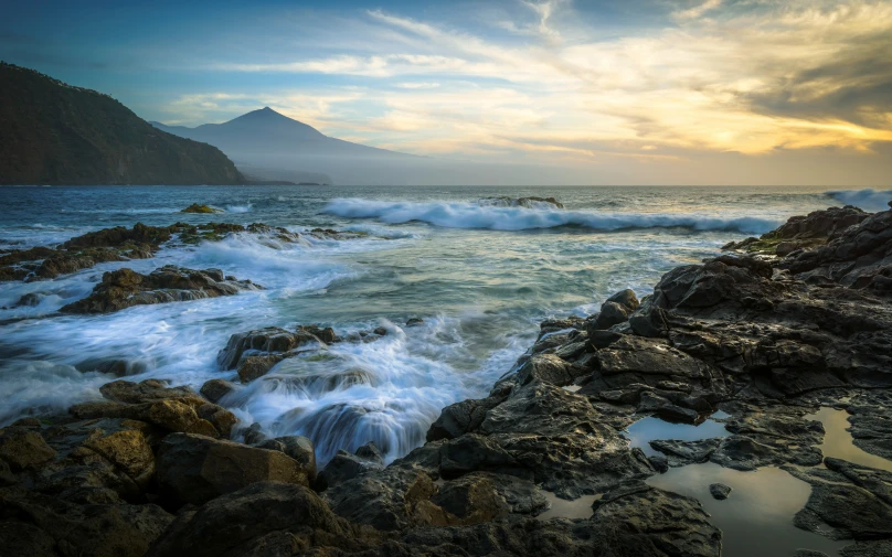 some waves crashing against the rocks and a mountain