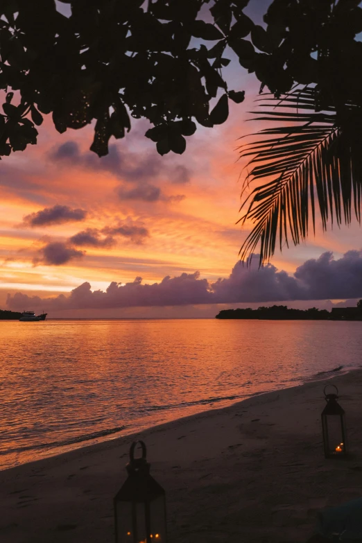 a view of a beach at sunset with two lanterns in the foreground