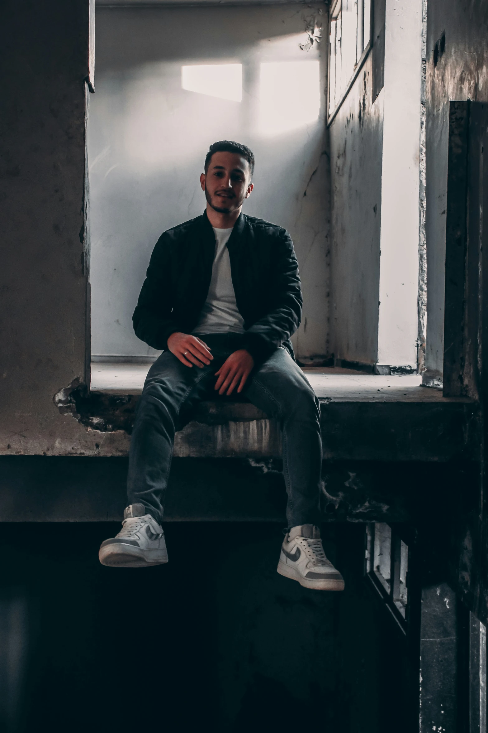 a young man in white shirt and black jacket sitting on the edge of a window sill