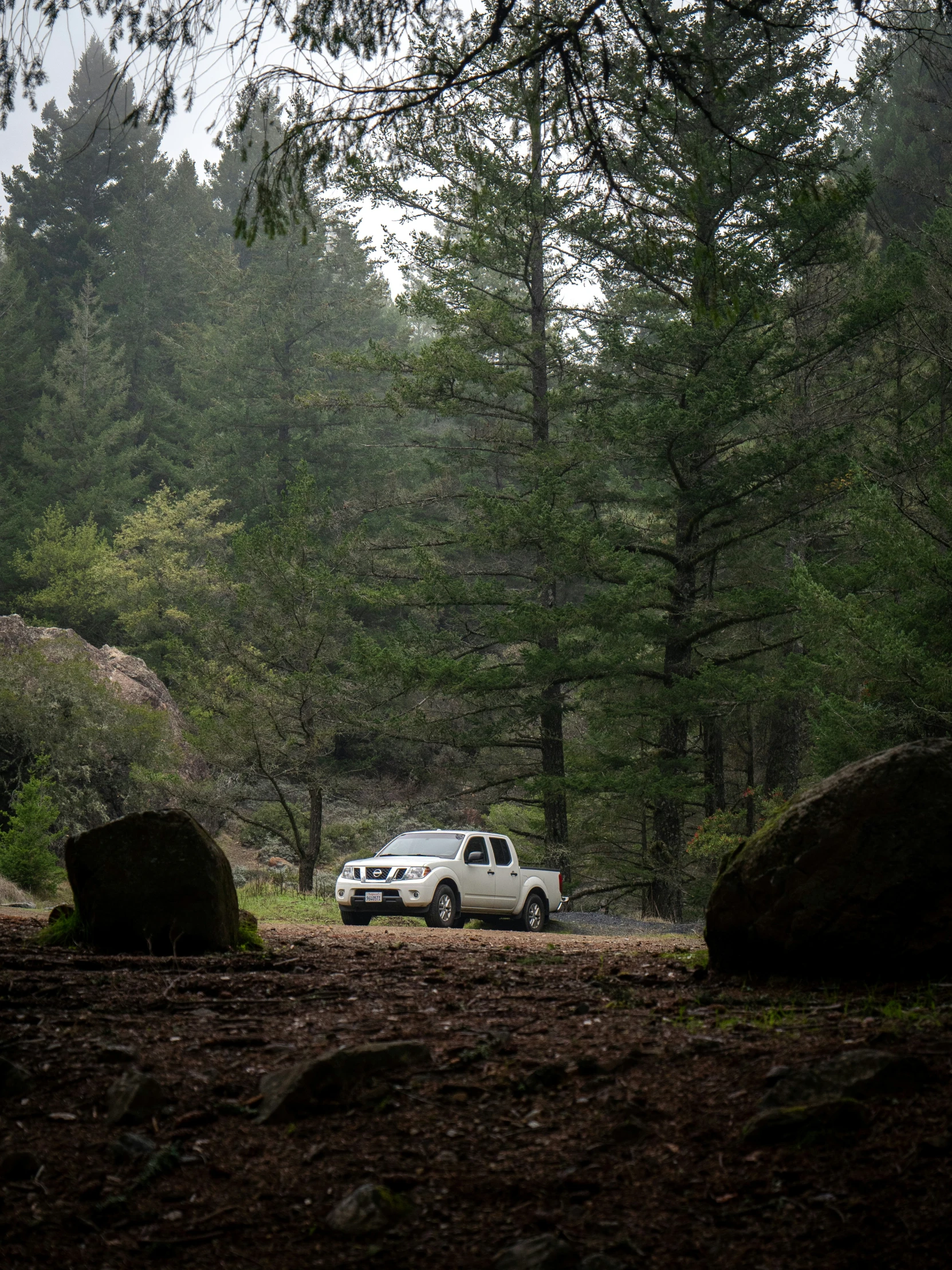 a pickup truck parked by large rocks in the woods