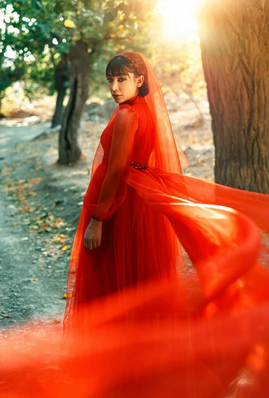 woman in a red dress and veil on the side of a dirt road