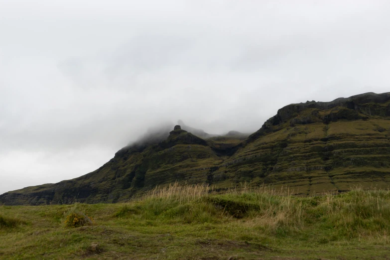 a large grassy area with some mountains covered in low hanging clouds