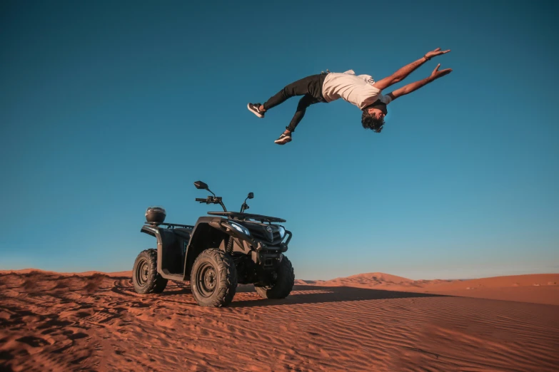 a man flying in the air above a four - wheeler in sand dunes