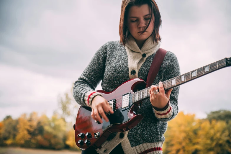 a  wearing a wool vest playing on an electric guitar