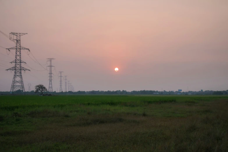 the sun rising over a field in an rural area