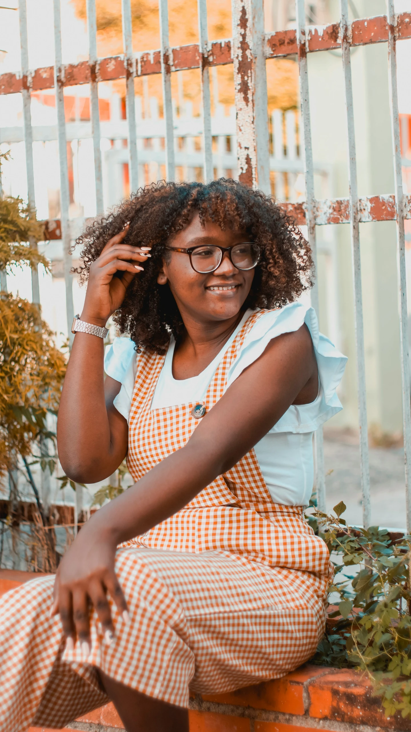 a woman sitting on a ledge smiling wearing glasses