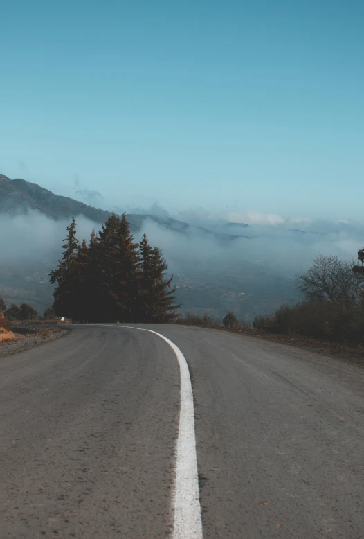 an empty street next to a mountain covered in clouds