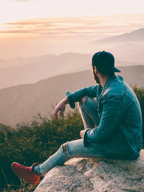 a man sitting on a large rock at sunset