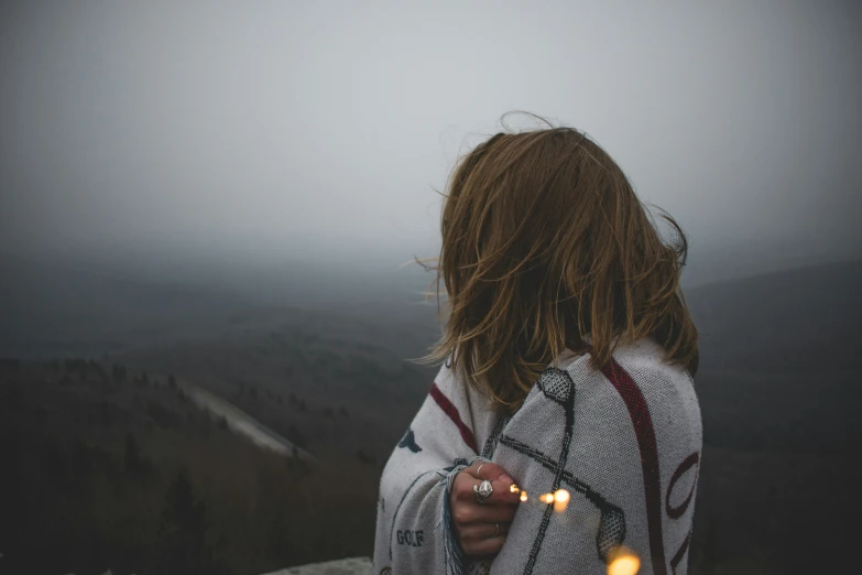 woman standing with hair blowing in the wind overlooking a mountain