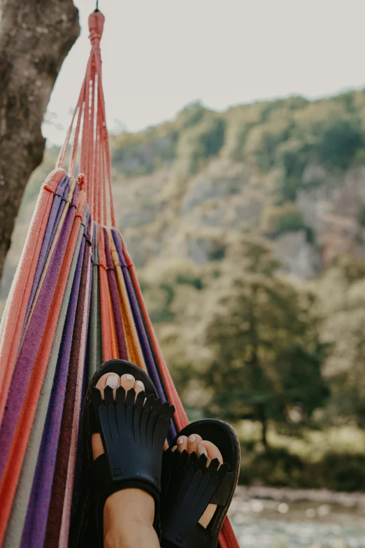 person with black shoes on in a hammock by some water