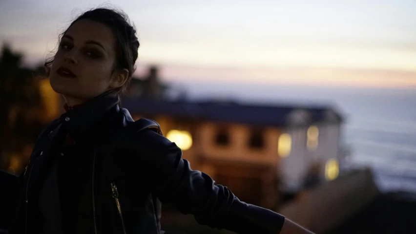 a woman poses outside at sunset with the ocean in the background