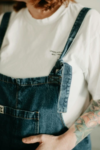 a man with tattoos wearing overalls and a white shirt