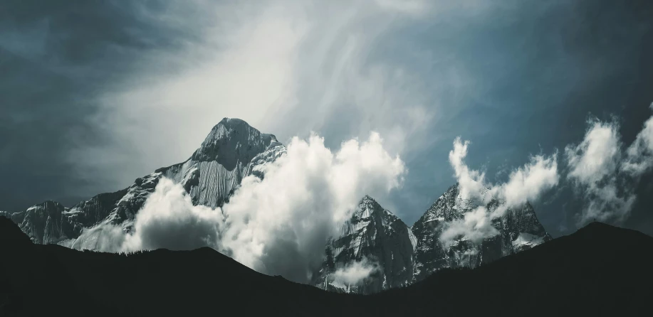 the top of three mountain peaks against a cloudy sky