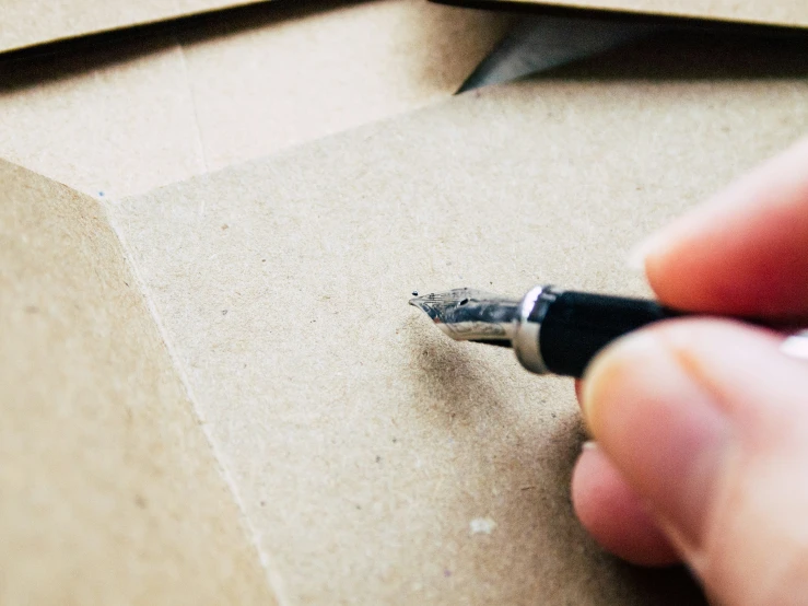 a hand with a black tip is writing a message on cardboard