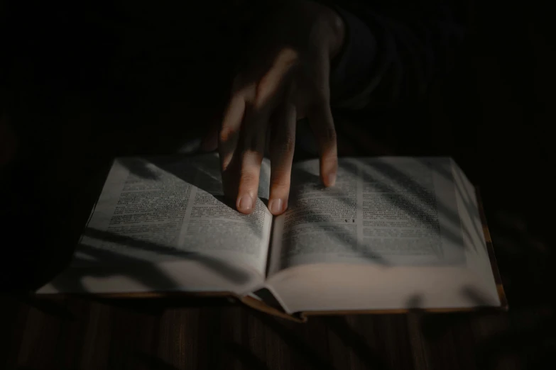 hands on top of an open book in the dark