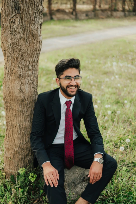 a man wearing a tie is sitting against a tree