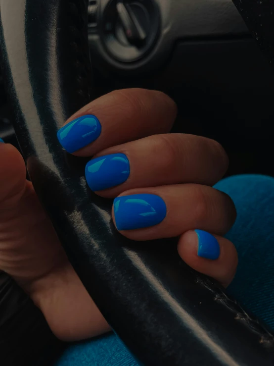 a woman with bright blue nail polish holding onto the steering wheel