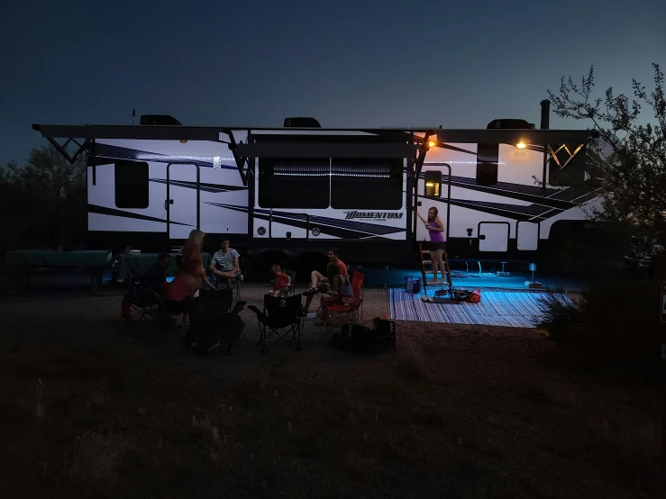 people sitting in chairs near a rv parked on the grass