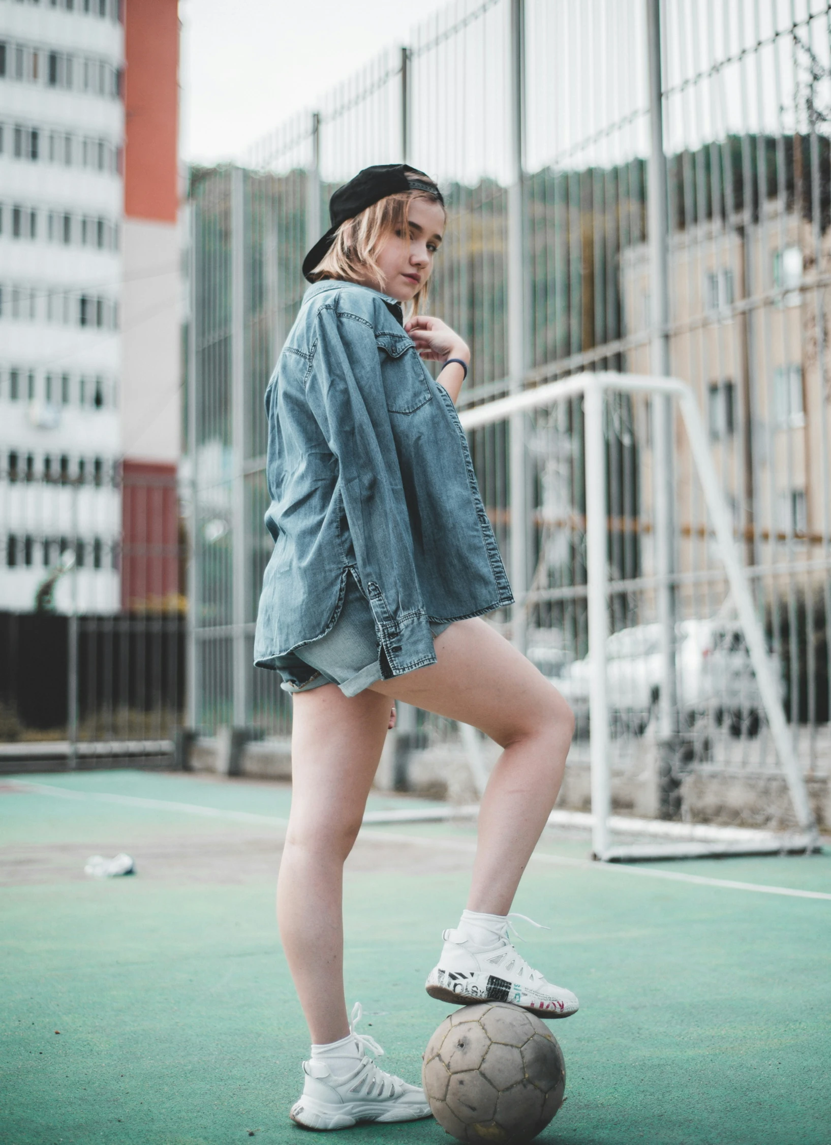 a woman wearing a denim jacket is leaning on a soccer ball