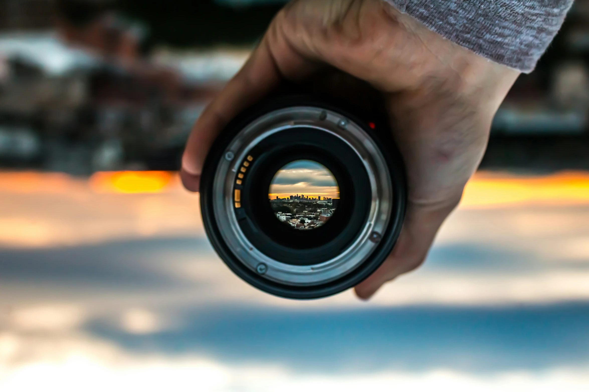 a camera lens held in a hand looking at a sunset