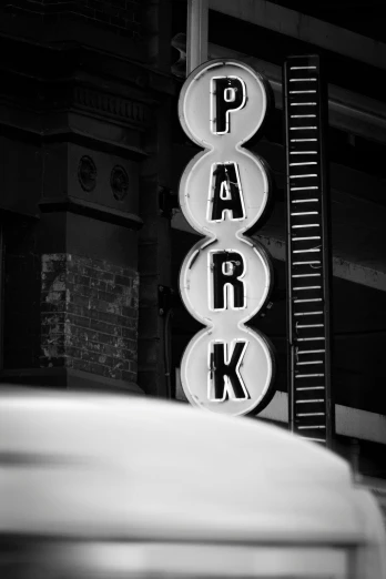 a park sign in a city with cars in the background