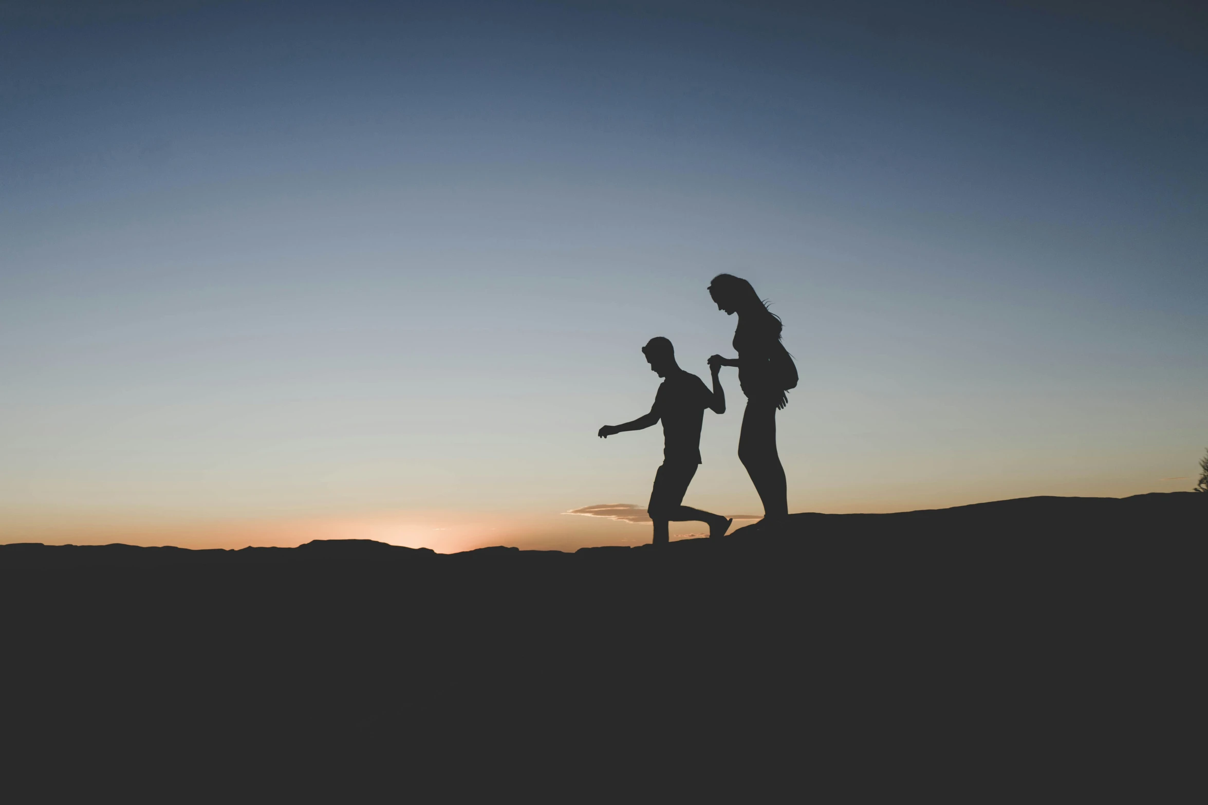 a silhouetted couple are walking through the hills during sunset