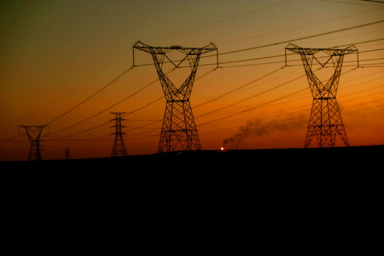 an electric power line with multiple poles against a sunset