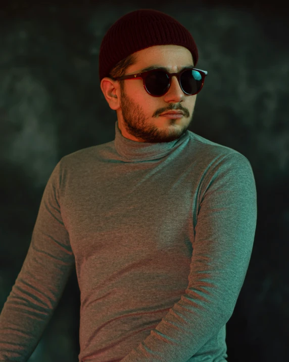 a man with dark glasses on wearing a gray sweater and a beanie
