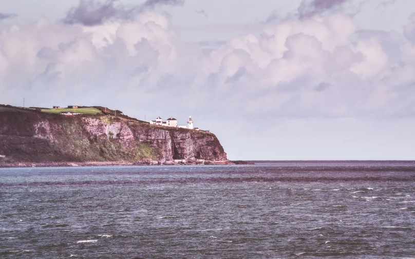 a small hill near the ocean under a cloudy blue sky