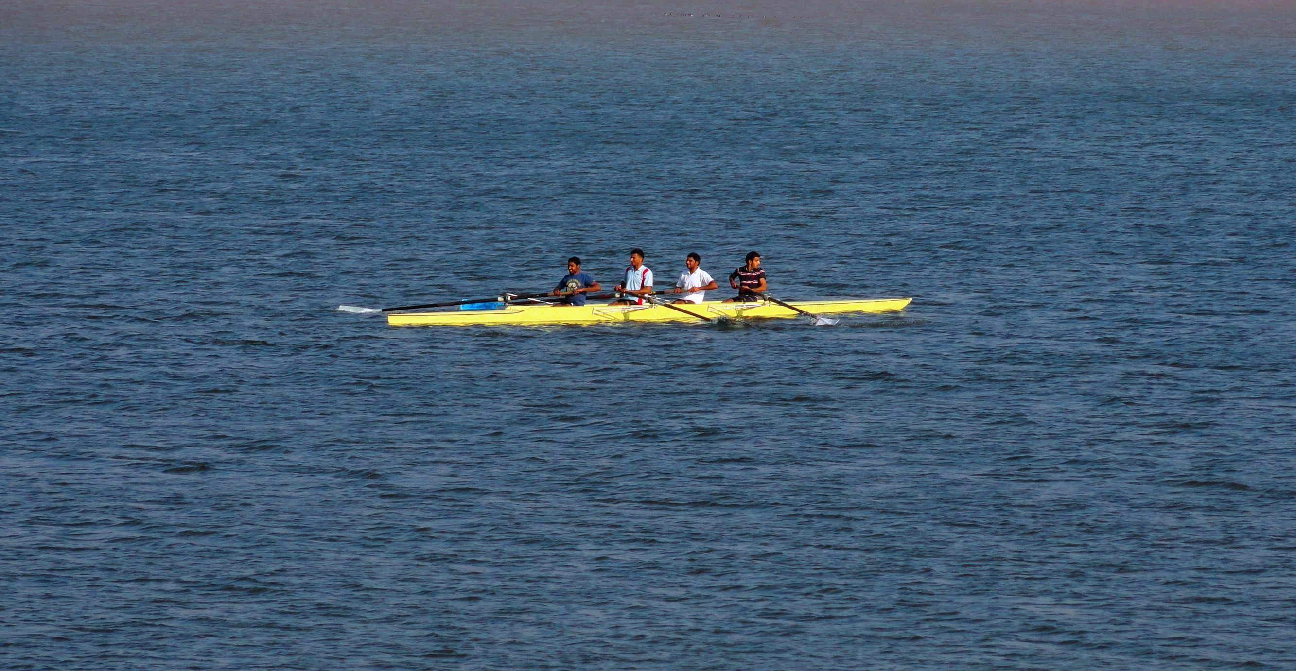 three people rowing on a long yellow paddle boat