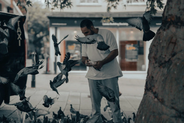 an old po of a man in white shirt feeding pigeons