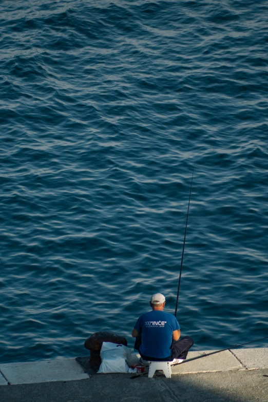 a person sitting on a sidewalk next to the water