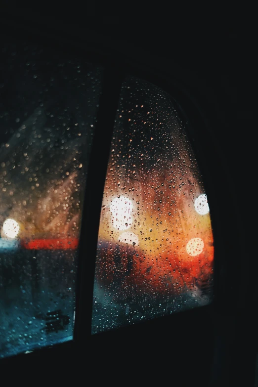 a car window covered in rain drops with city lights seen through the window