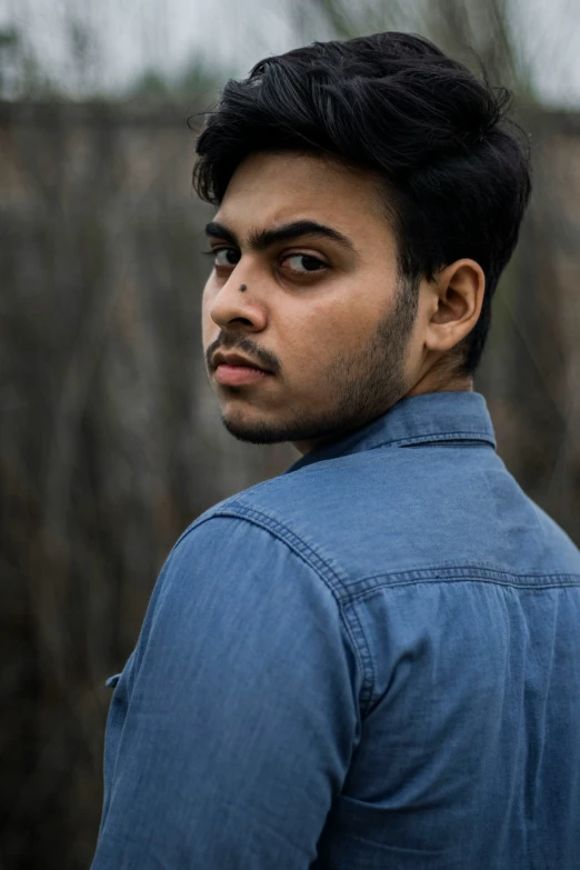 man with short dark hair in blue denim shirt looking away