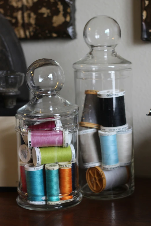 some jars filled with sewing thread and spools of thread