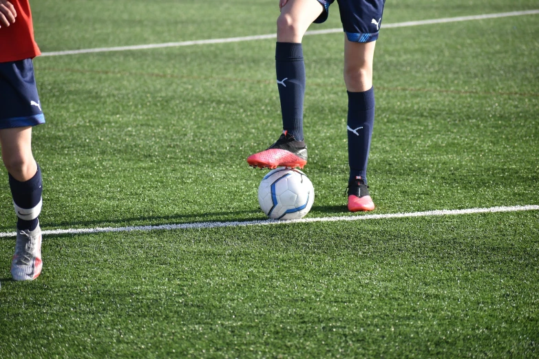 two girls in blue uniforms are kicking a soccer ball