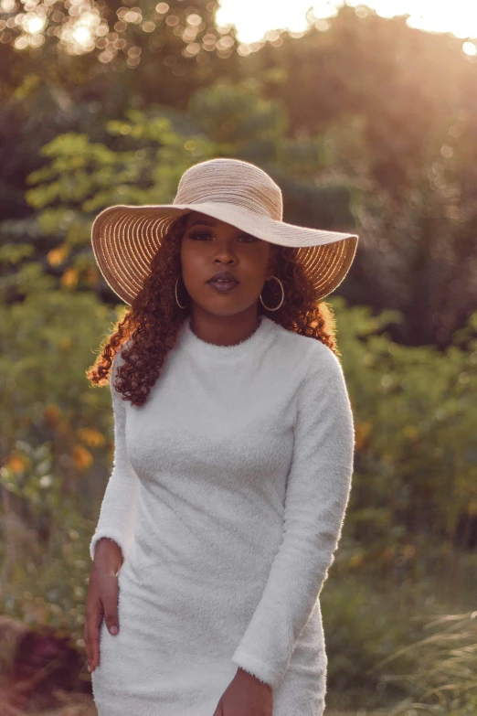 a woman standing in the middle of a field wearing a hat and sweater