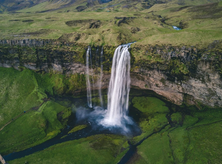 a waterfall surrounded by grass and some hills