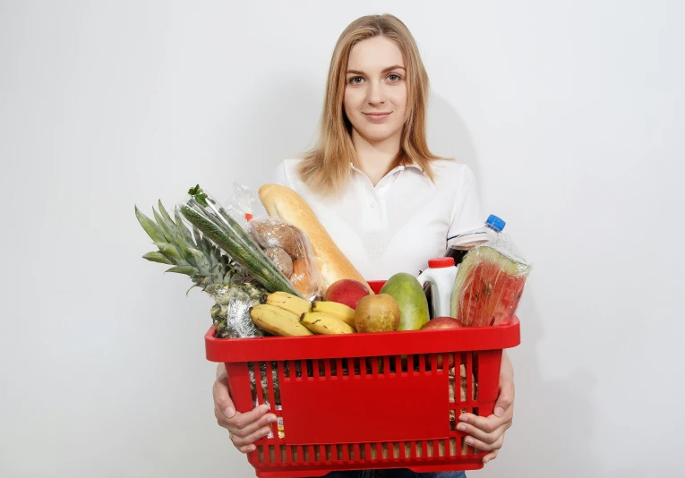 a woman holding a red basket filled with fresh fruits and vegetables