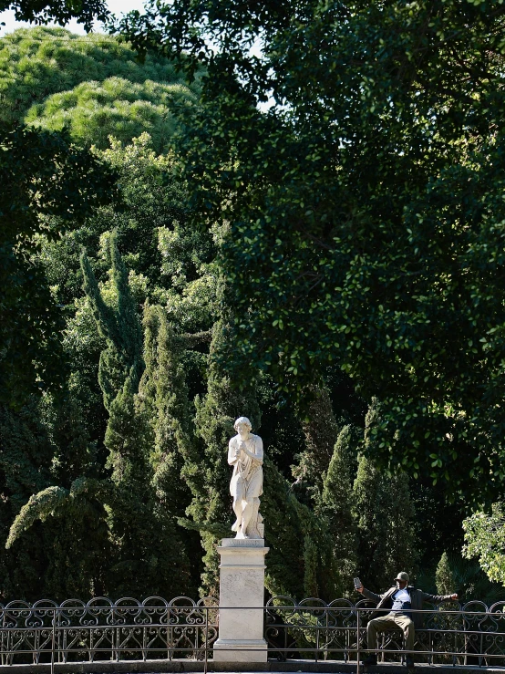 a white statue surrounded by trees is near a small building