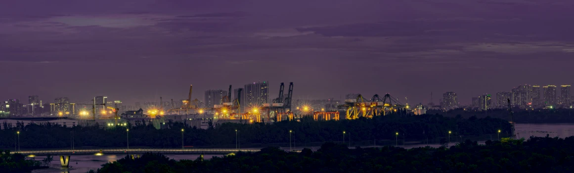 some buildings a bridge and trees water purple lights and clouds